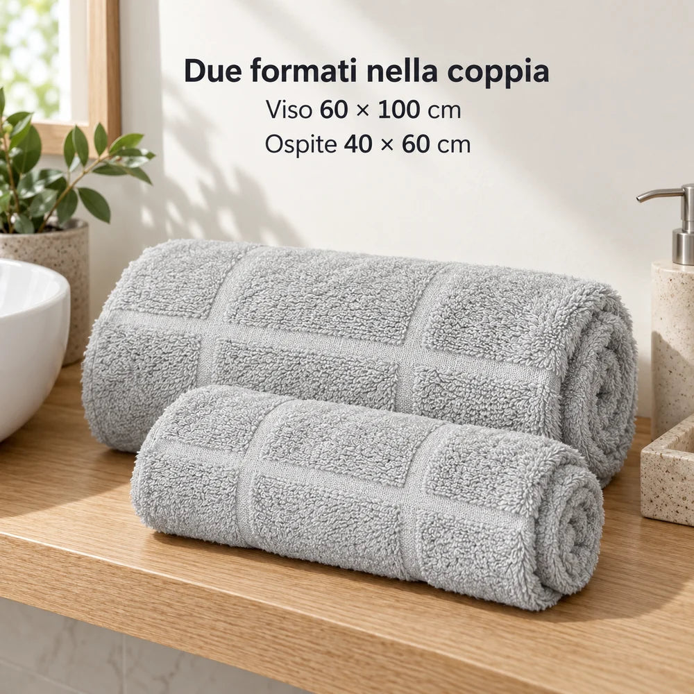 Due asciugamani Perla arrotolati separatamente: viso 60 × 100 cm e ospite 40 × 60 cm. Foto illustrativa: Perla. Arredi e accessori esclusi.