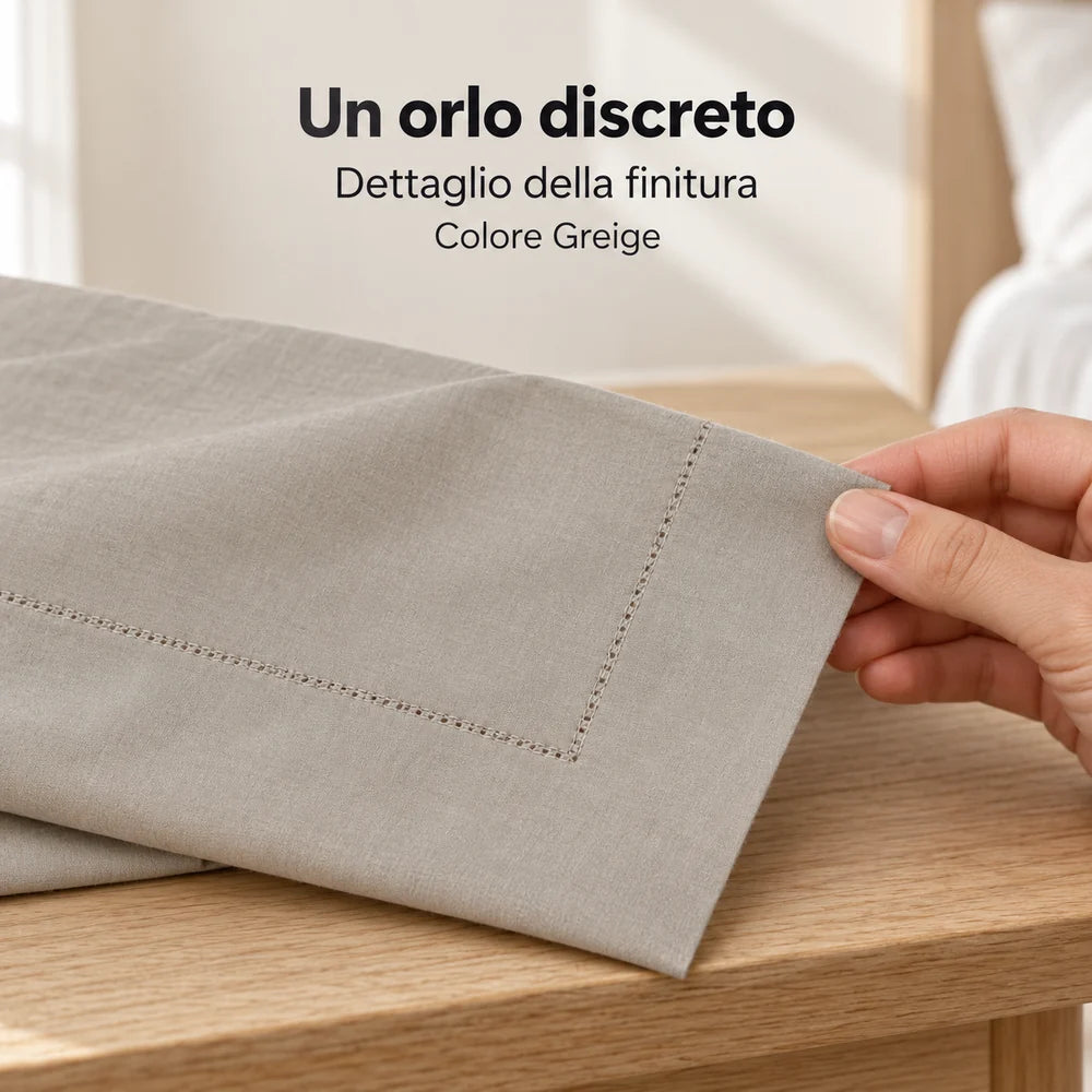 Angolo Greige con sottile orlo a giorno, sollevato leggermente da una mano. Foto illustrativa: Greige. Guanciali, arredi e accessori esclusi.