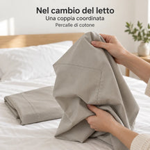 Una federa Greige raccolta fra le mani, la seconda ripiegata sul letto. Foto illustrativa: Greige. Guanciali, arredi e accessori esclusi.